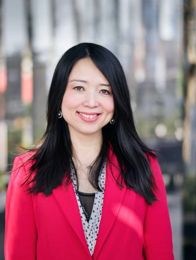 A smiling headshot of Dr. Chen Mao Davies, Founder and CEO of Anya. She has long dark hair, and is wearing a vibrant magenta blazer over a polka-dotted blouse. She is looking directly at the camera in front of an urban background.